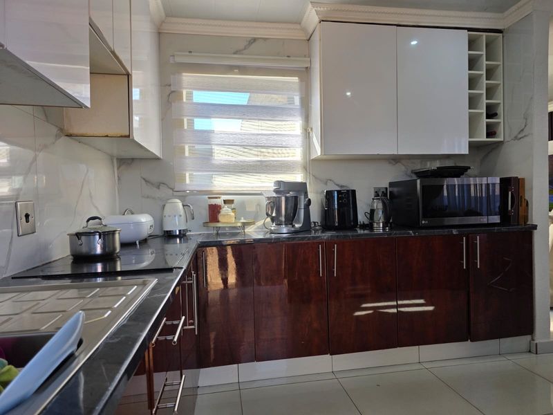 Modern kitchen featuring high-gloss cabinetry, marble-effect splashbacks, stone countertops, and integrated storage solutions with clean ceramic floor tiling.