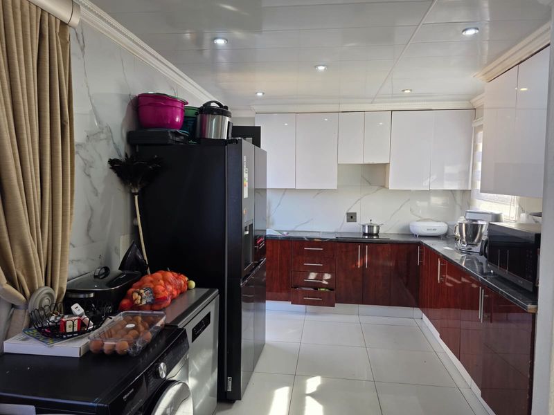 A functional kitchen featuring high-gloss cabinetry, marble-effect wall finishes, and tiled flooring, offering a clean and modern aesthetic.