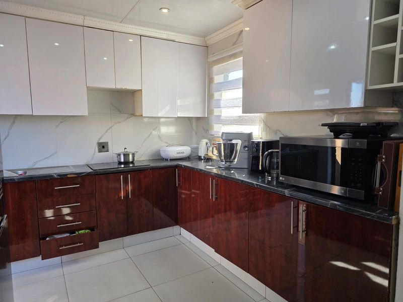 Modern kitchen featuring high-gloss two-tone cabinetry, marble-effect splashback, stone countertops, and integrated hob, offering a clean and functional culinary space.