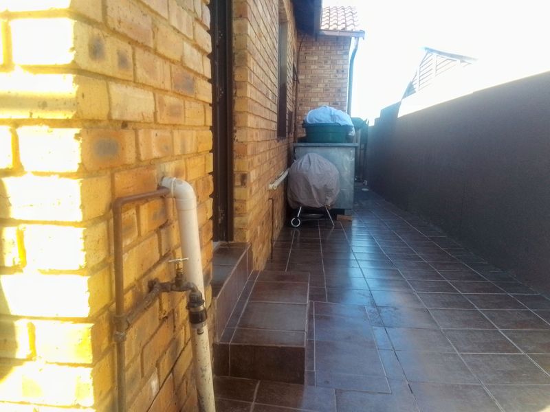 A side passage or rear exterior area featuring face brick walls and tiled flooring with an external water tap.