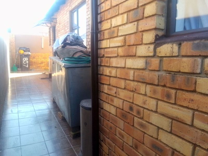 A narrow side or rear exterior walkway featuring brick walls and tiled flooring with a drainage downpipe.