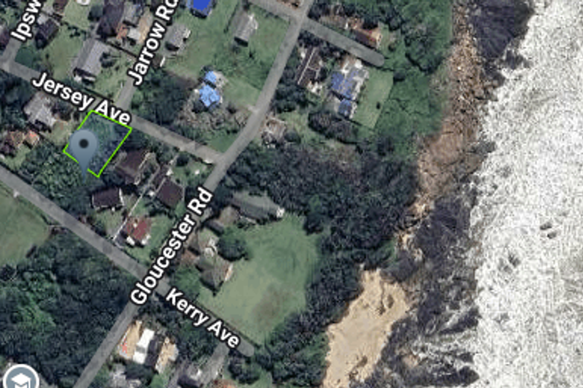 Aerial view of a vacant residential plot located near the coastline, showing surrounding street layout and neighborhood context.