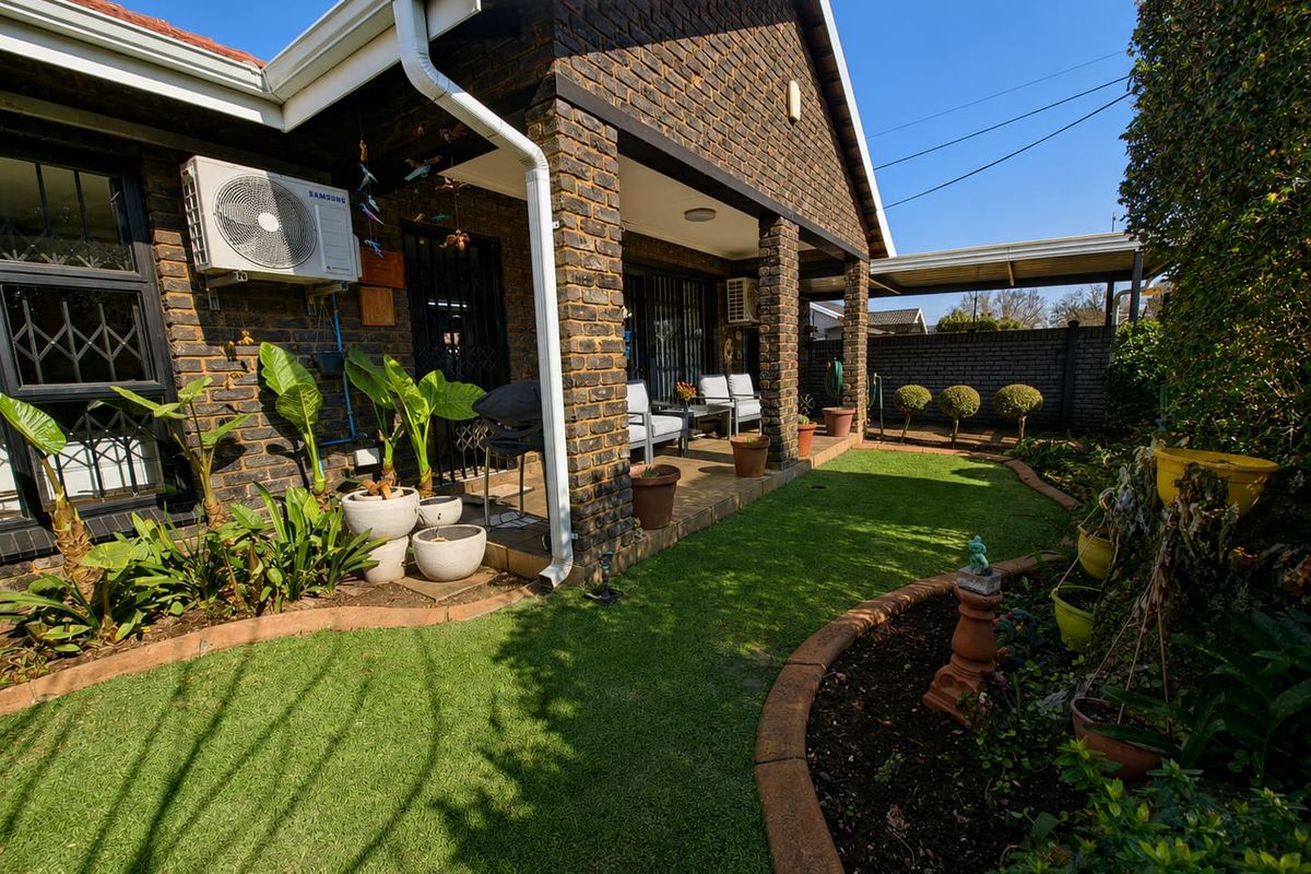 A well-maintained rear exterior view featuring a covered brick patio, landscaped garden, and secure access points to the main dwelling.