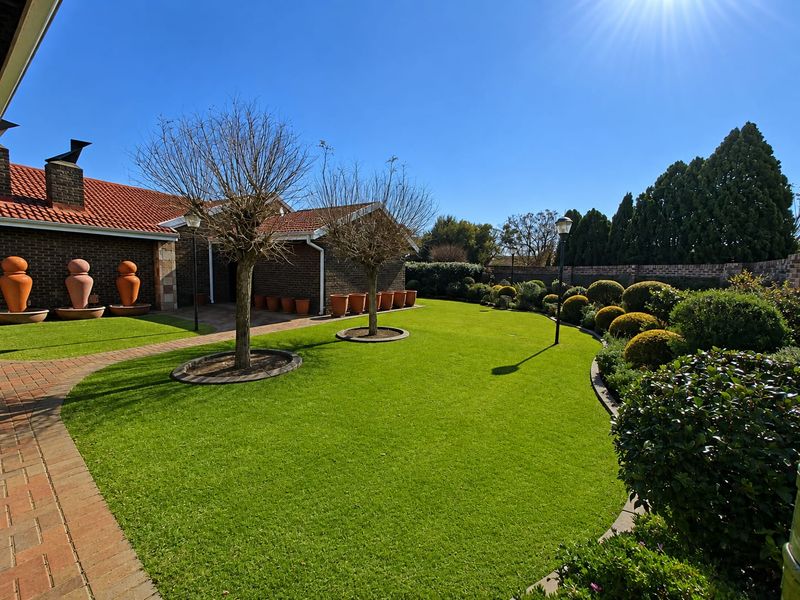 A well-maintained garden featuring manicured lawn, mature trees, brick pathways, and a secure brick boundary wall, providing a neat and established outdoor space.