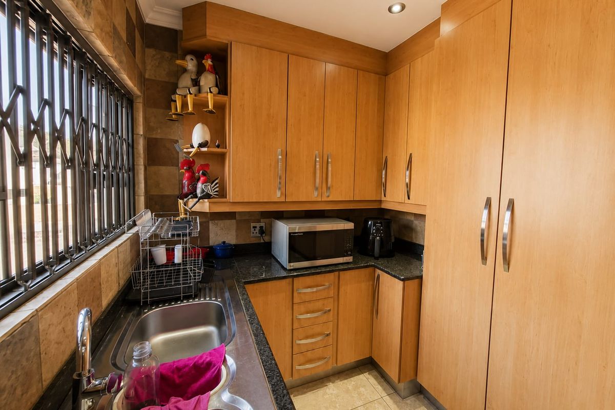 A functional kitchen featuring light wood cabinetry, granite countertops, a double stainless steel sink, and tiled finishes throughout.