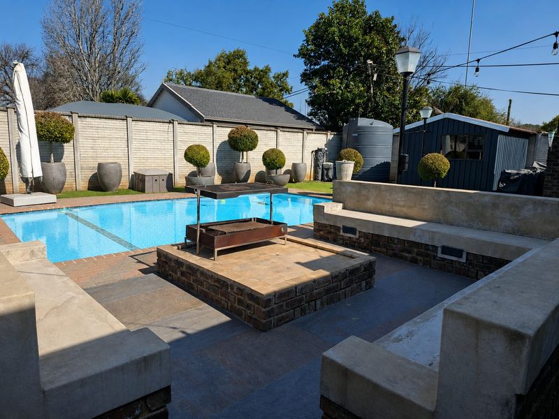 Outdoor entertainment area featuring a swimming pool, built-in concrete seating, and a central brick fire pit, perfect for hosting and relaxation.