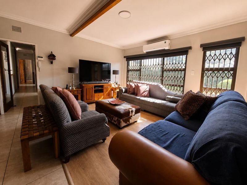 A comfortable living room featuring laminate flooring, coved cornicing, and security gates on the windows, equipped with a wall-mounted split-system air conditioner.
