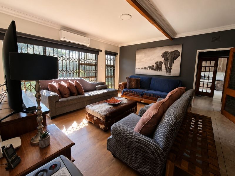 A comfortable living room featuring laminate flooring, decorative ceiling beams, and large windows secured with metal security gates.