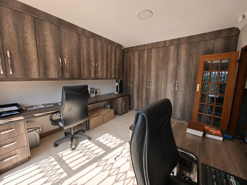 A functional home office featuring extensive built-in cabinetry, a spacious integrated desk, and tiled flooring, providing ample storage and workspace.