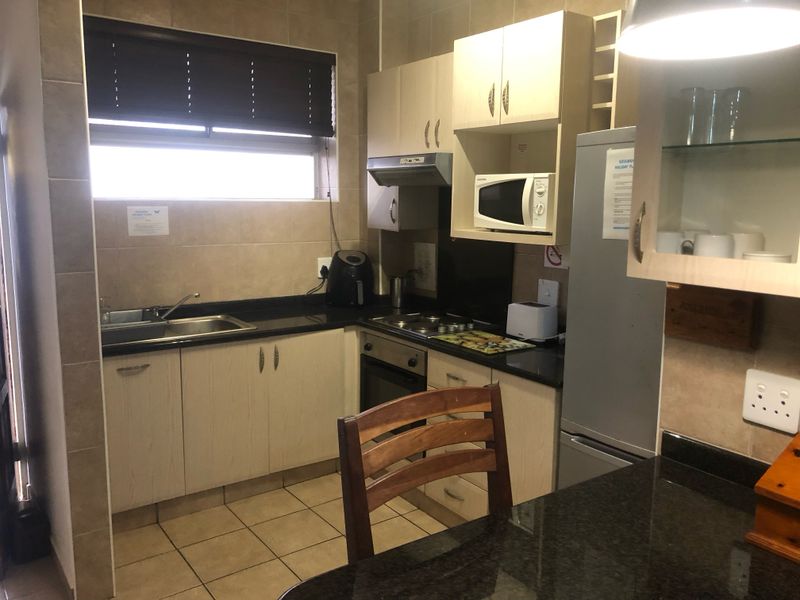 A functional kitchen featuring light wood cabinetry, dark granite countertops, tiled backsplash, and integrated appliances including an oven and hob.