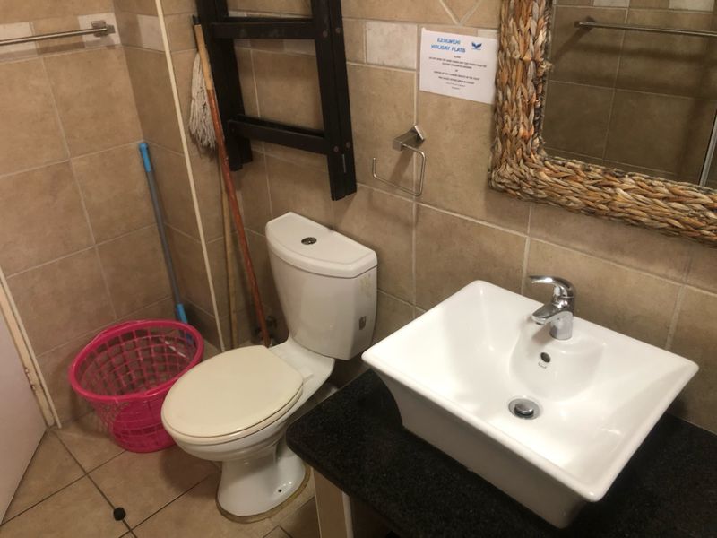 A functional bathroom featuring a vessel sink on a granite vanity, a standard toilet, and neutral ceramic wall and floor tiling.