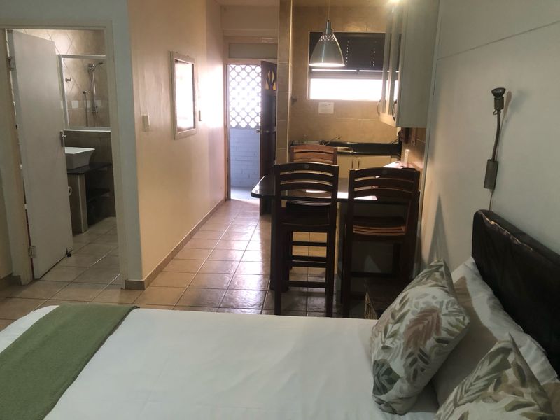 Open-plan studio apartment featuring a compact kitchen area, tiled flooring throughout, and an adjoining bathroom with a shower.