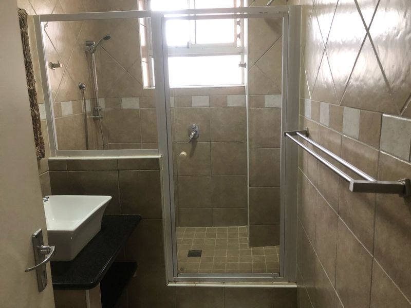 A compact bathroom featuring a tiled shower enclosure, a vessel sink on a granite vanity top, and wall-mounted towel rails.