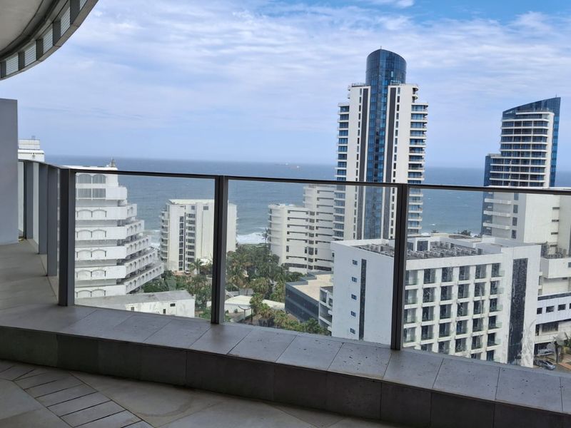 A spacious balcony featuring a modern glass balustrade and tiled flooring, offering expansive views of the surrounding city skyline and ocean.