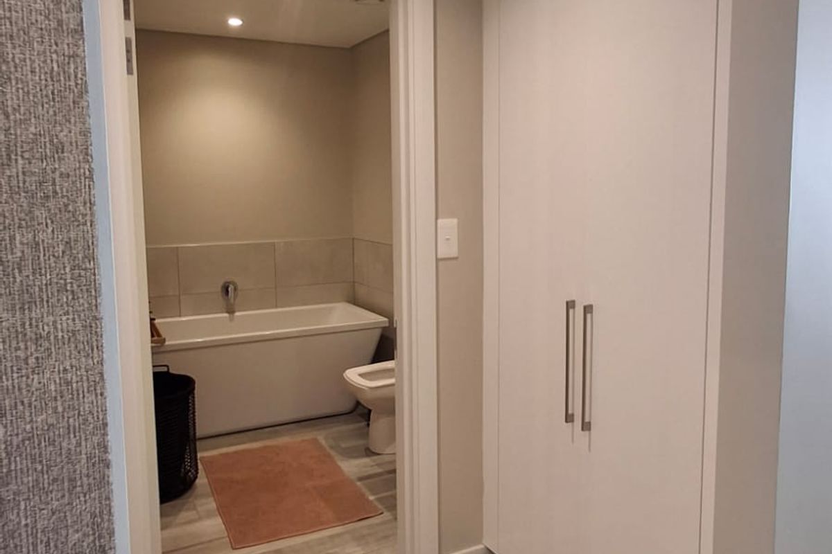 A modern bathroom featuring a bathtub, toilet, and built-in storage cupboards, finished with neutral tones and contemporary tiled flooring.