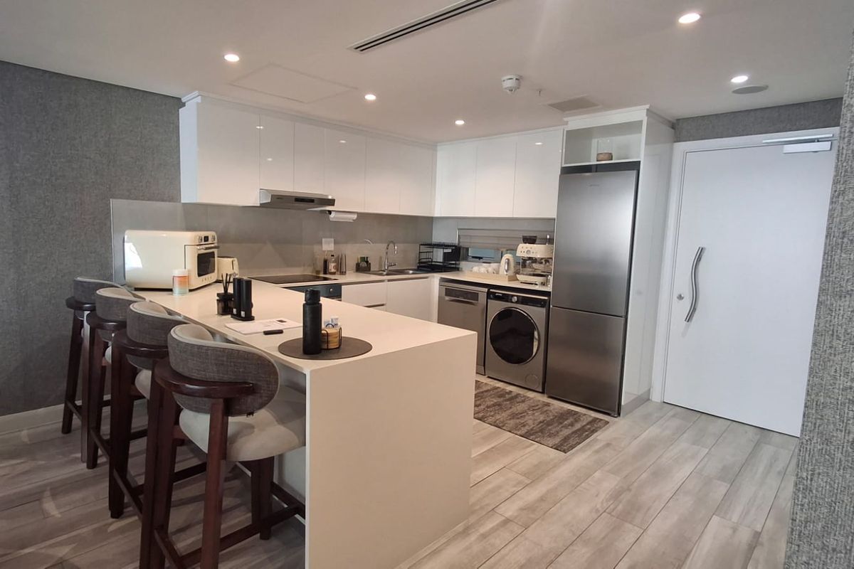 Modern kitchen featuring sleek white cabinetry, stone countertops, a breakfast bar, and integrated stainless steel appliances, including a washing machine and dishwasher.