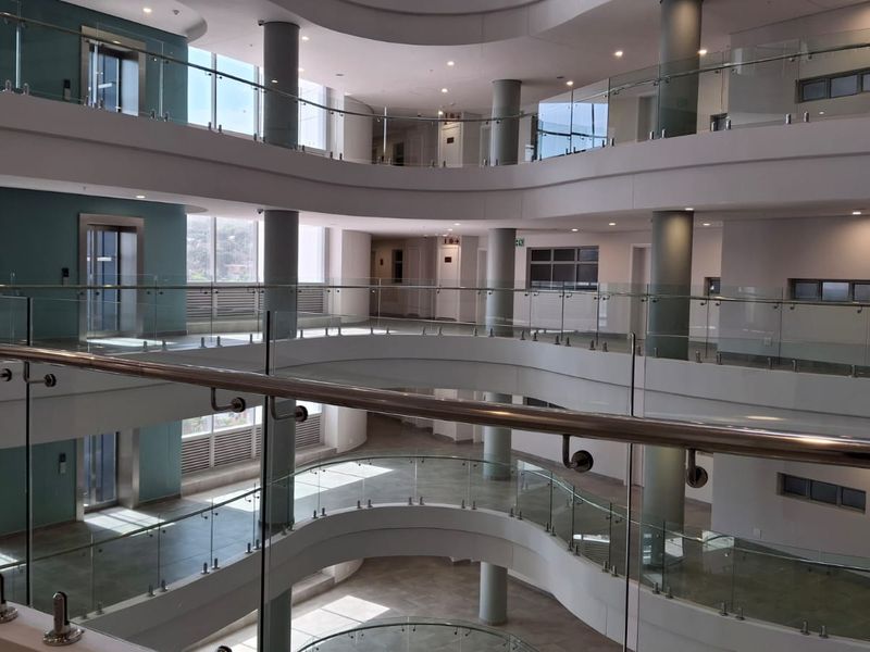 A modern, multi-level apartment building atrium featuring curved walkways, glass balustrades, and structural columns with integrated elevator access.