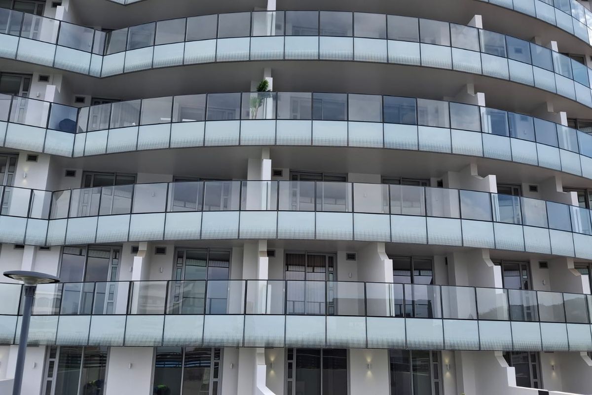 A modern apartment building facade featuring multiple levels of private balconies with sleek glass balustrades and large sliding glass doors.