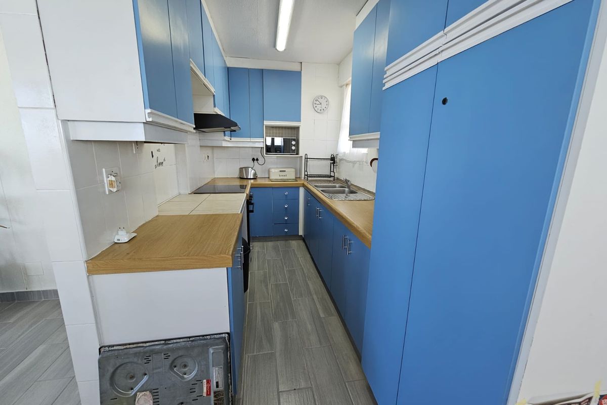 A functional galley-style kitchen featuring blue cabinetry, wood-look laminate countertops, tiled backsplash, and modern grey floor tiles.