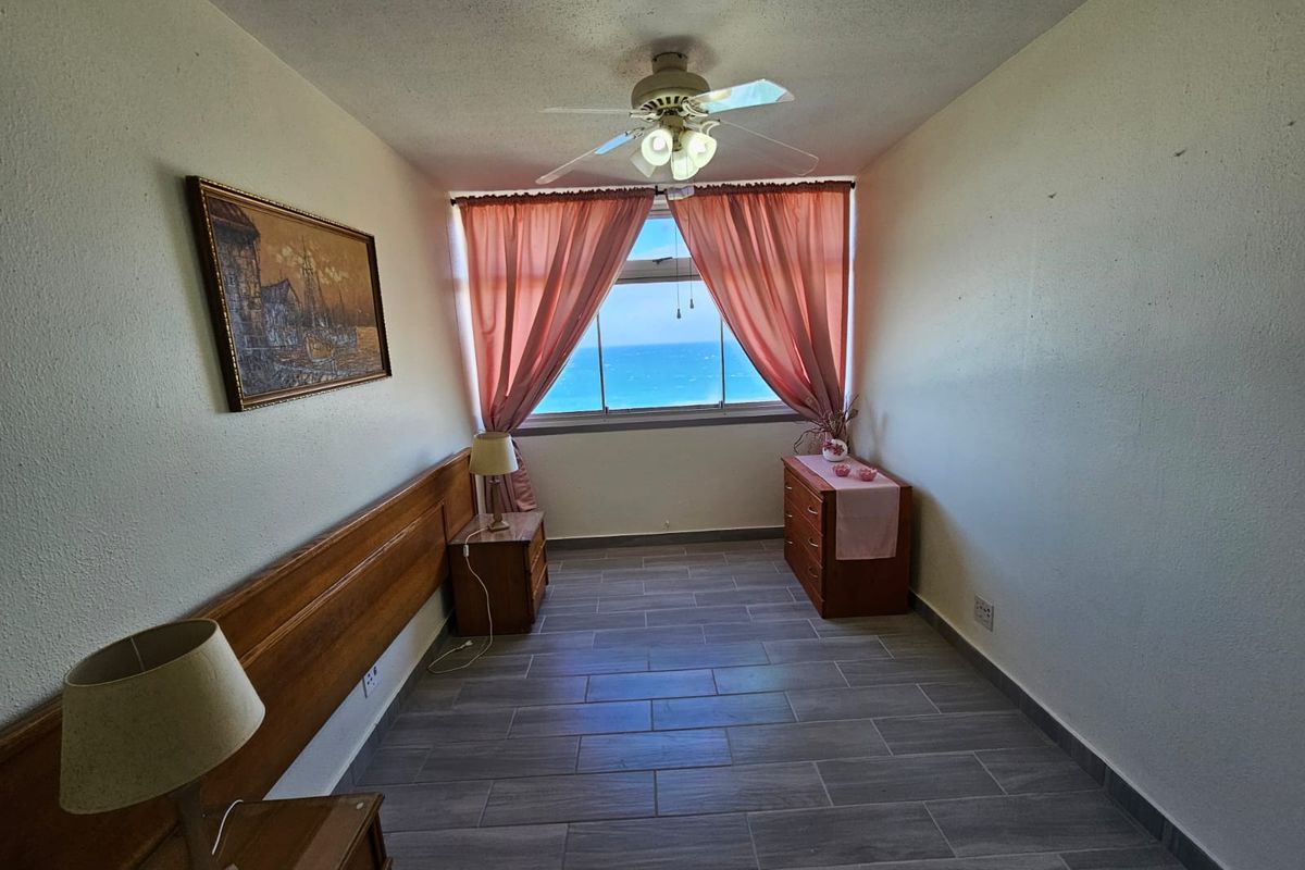 A bedroom featuring tiled flooring, a ceiling fan, and a built-in headboard, offering a direct view of the ocean.