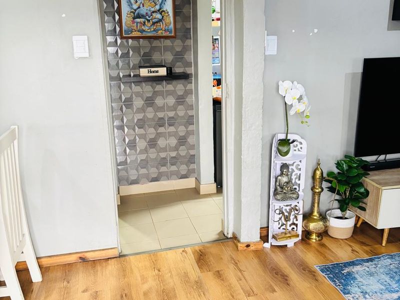 A living area featuring laminate flooring and a transition into a secondary space with decorative textured wall tiles.
