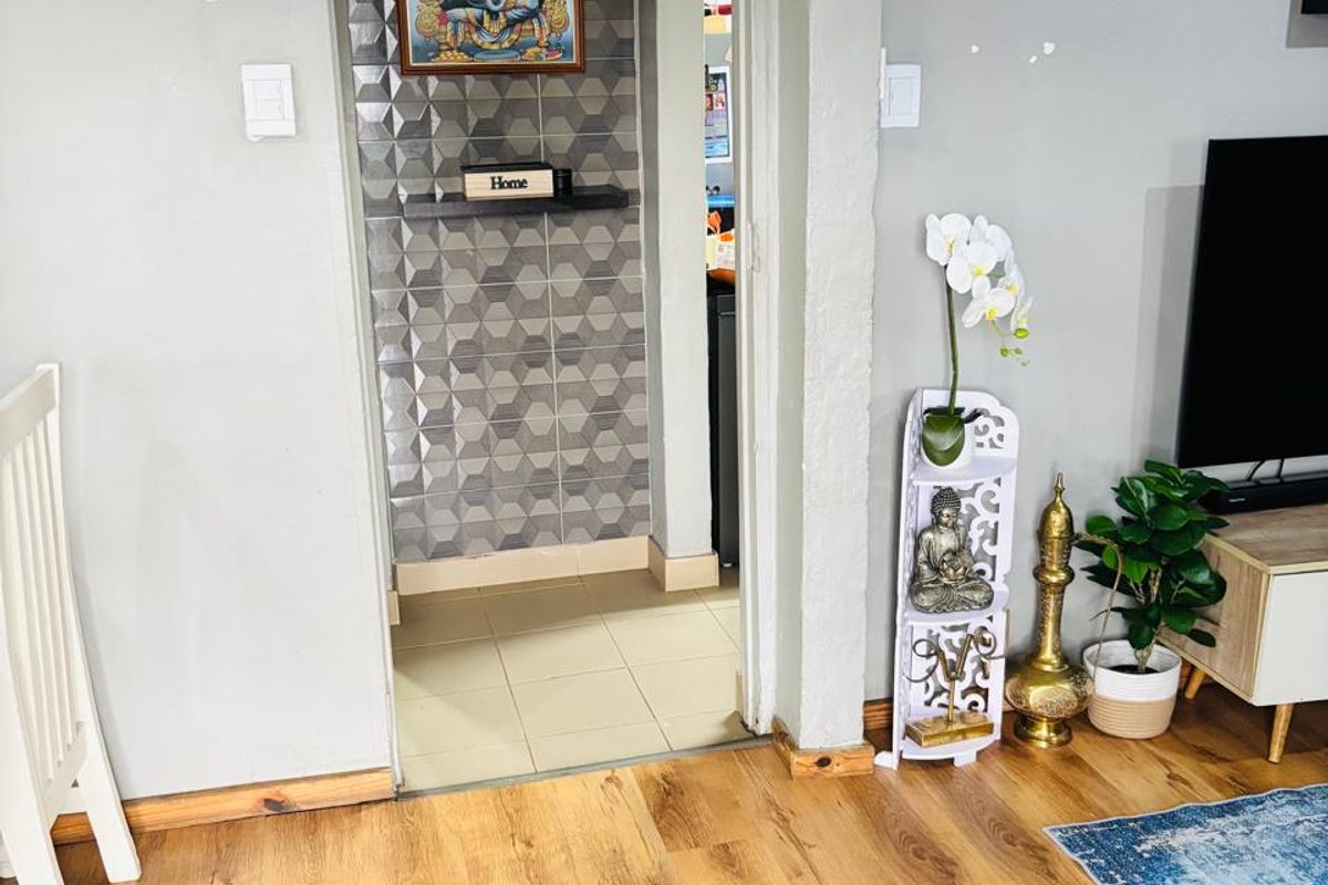 A living area featuring laminate flooring and a transition into a secondary space with decorative textured wall tiles.