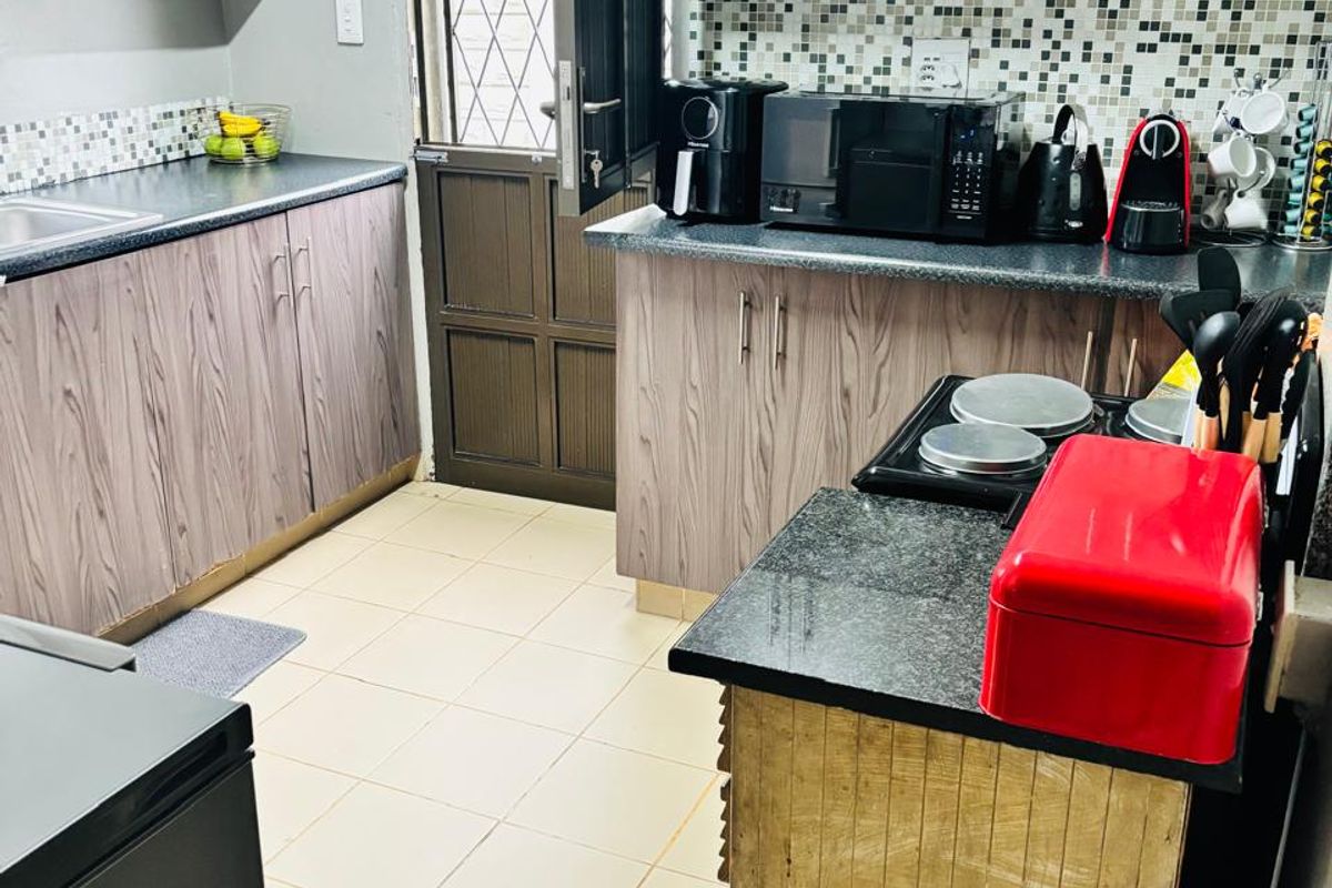 Functional kitchen featuring wood-look laminate cabinetry, granite countertops, mosaic tile backsplash, and direct access to the exterior via a security door.