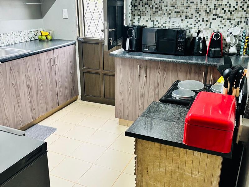 Functional kitchen featuring wood-look laminate cabinetry, granite countertops, mosaic tile backsplash, and direct access to the exterior via a security door.