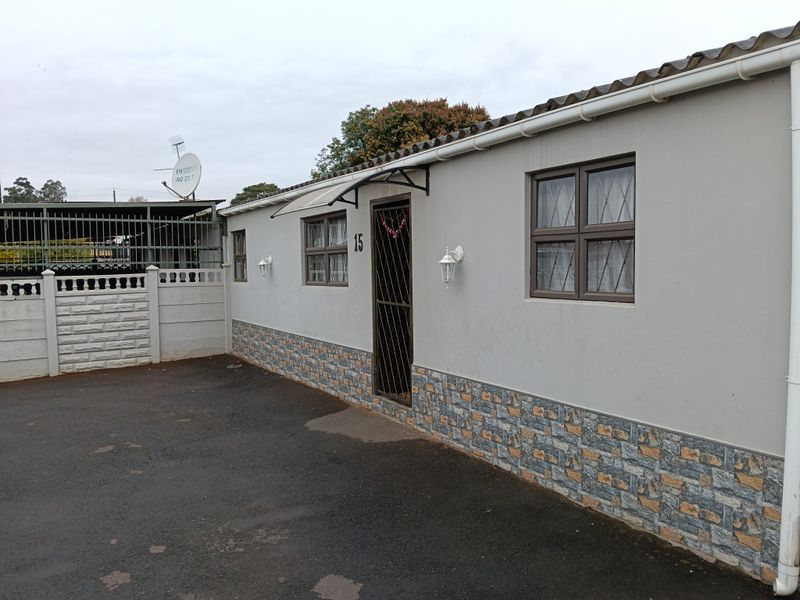 Front exterior view of the townhouse featuring a paved driveway, security gate entrance, stone-clad base, and well-maintained exterior walls with fitted lighting.