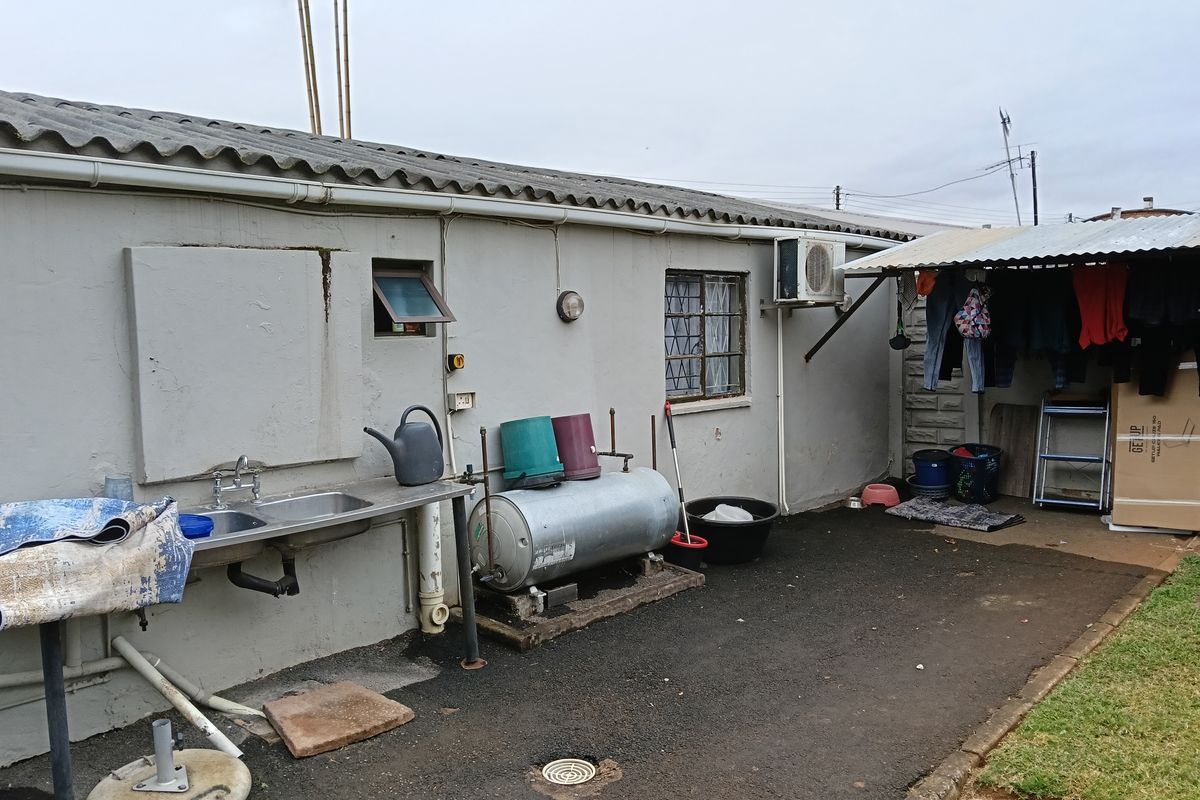 Rear exterior area featuring a utility sink, electric water heater, and a covered outdoor space with a corrugated metal roof.