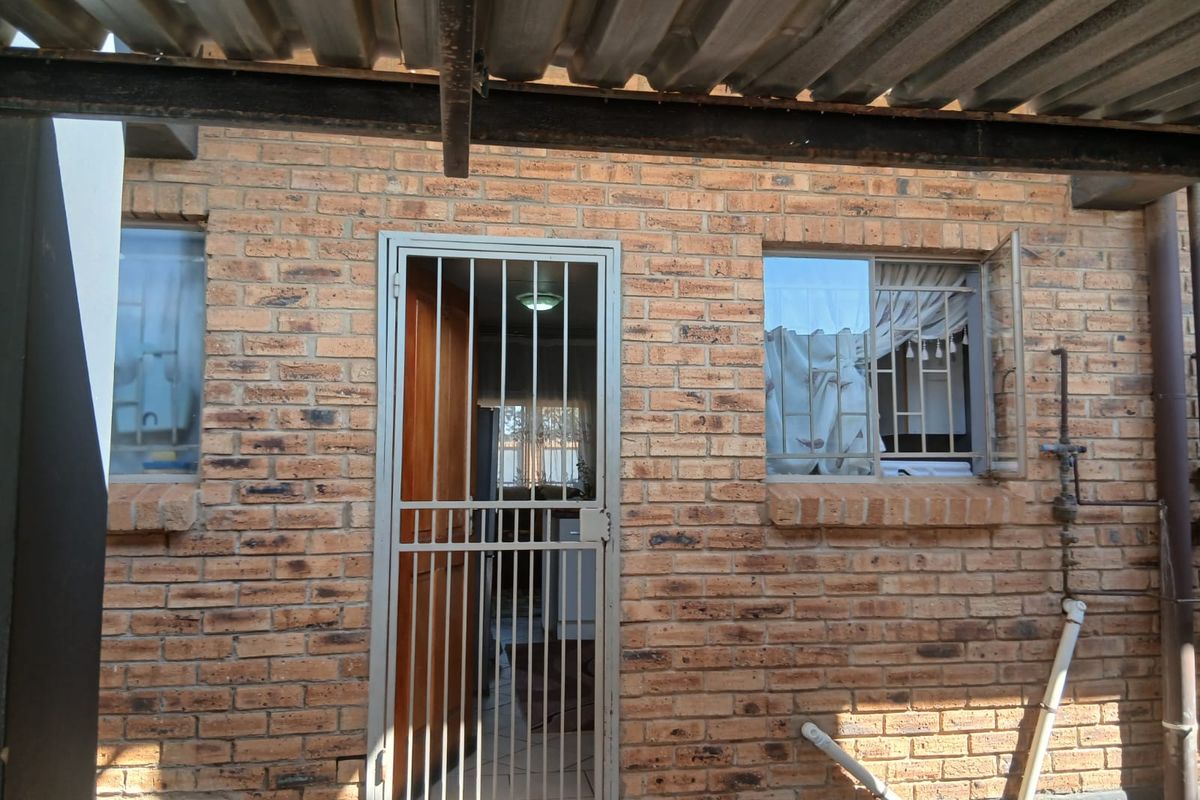 Rear exterior view of the townhouse featuring face brick walls, a security gate, and a corrugated metal roof covering.