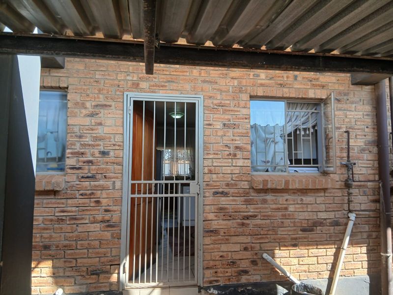 Rear exterior view of the townhouse featuring face brick walls, a security gate, and a corrugated metal roof covering.