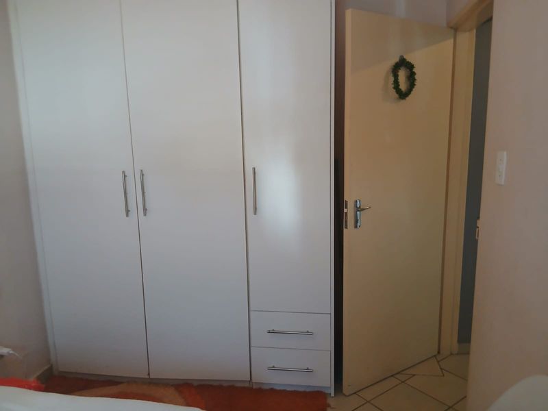 A bedroom featuring a white built-in wardrobe with integrated drawers and tiled flooring.