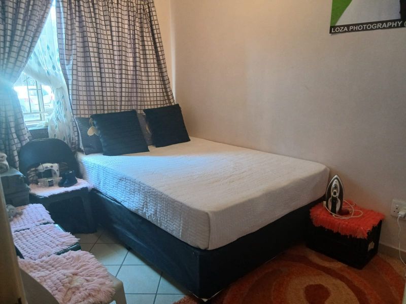 A compact bedroom featuring tiled flooring and a window fitted with security bars.