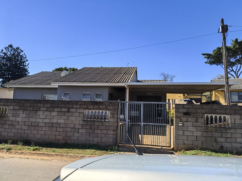 Front exterior view of the property featuring a concrete block boundary wall, metal security gate, and a covered carport area.