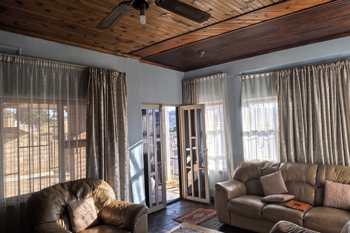 A living room featuring a timber tongue and groove ceiling, ceiling fan, tiled flooring, and multiple windows providing natural light and access to the exterior.