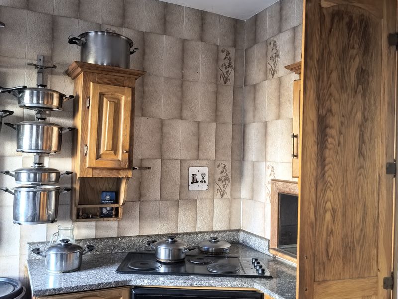 A compact kitchen featuring wooden cabinetry, granite countertops, a built-in oven, and an electric hob with a decorative tiled backsplash.