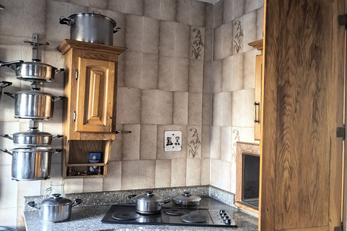 A compact kitchen featuring wooden cabinetry, granite countertops, a built-in oven, and an electric hob with a decorative tiled backsplash.