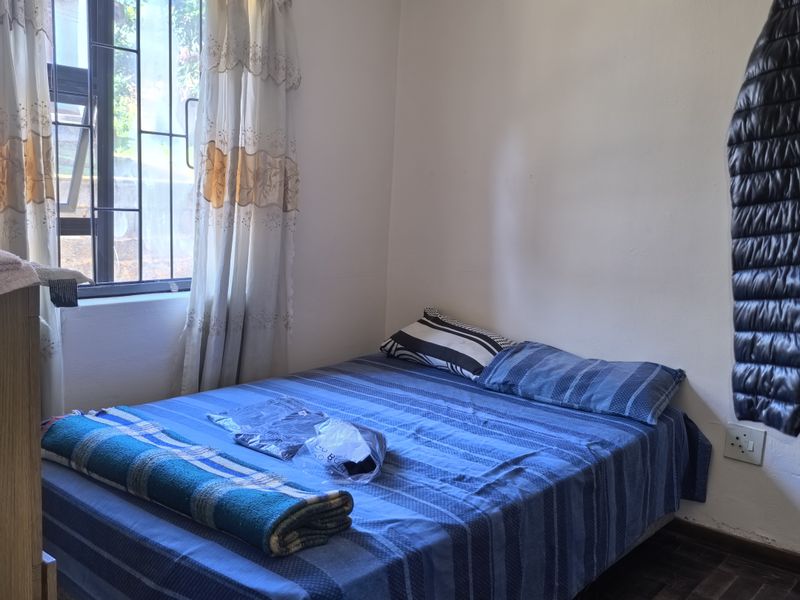 A functional bedroom featuring classic parquet flooring, a window with security bars, and an integrated ceiling air vent.