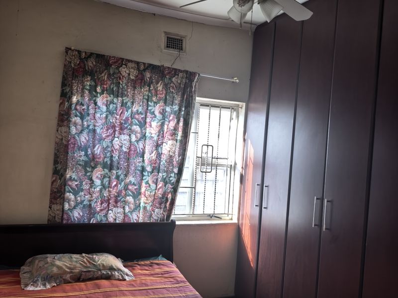 Bedroom featuring built-in dark wood cupboards, a ceiling fan, and security bars on the window. The room requires cosmetic updates to the walls and ceiling.