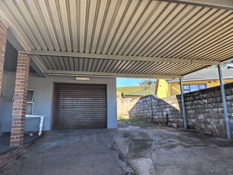 A covered carport area featuring a roller shutter garage door, concrete flooring, and a brick boundary wall.