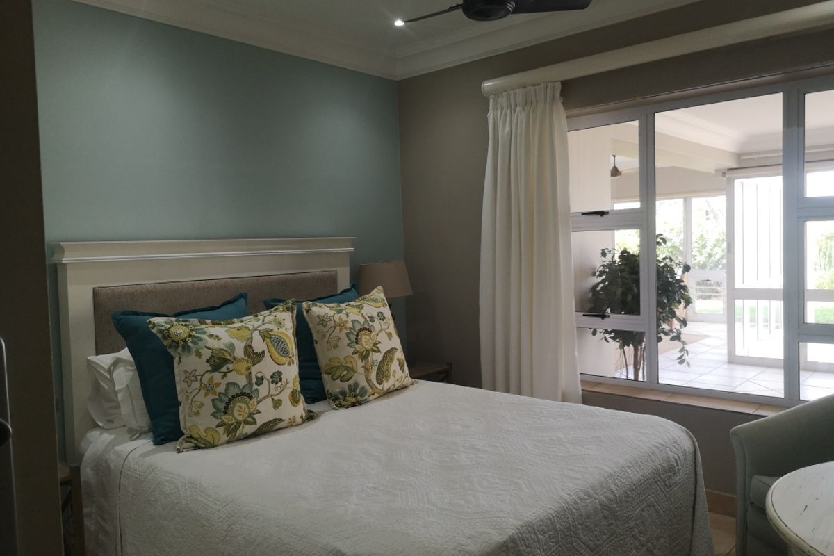 A well-maintained bedroom featuring a ceiling fan, crown molding, and a large window providing natural light and a view of the patio.