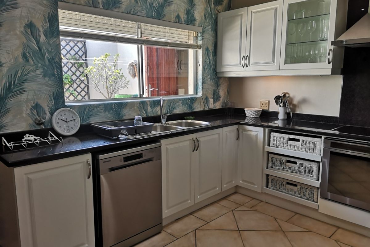 A functional kitchen featuring white cabinetry, dark granite countertops, built-in oven, extractor fan, and tiled flooring with a view to the exterior.