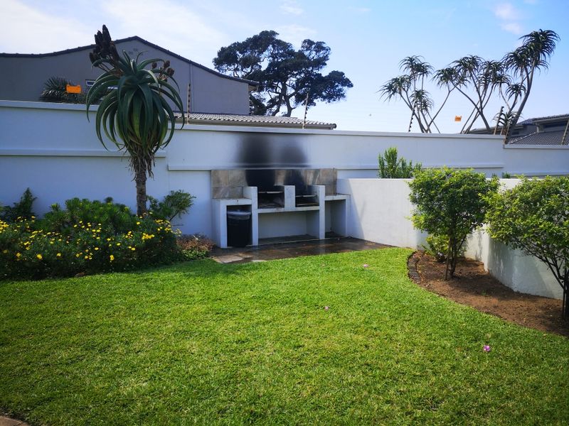 A well-maintained garden area featuring a built-in braai facility set against a boundary wall with established landscaping.