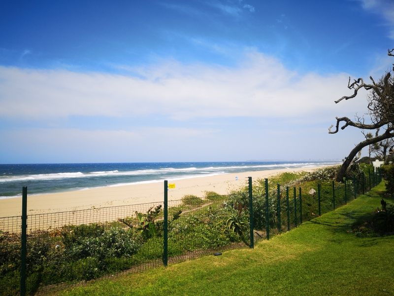 A scenic view of the coastline featuring a well-maintained lawn and a secure wire mesh perimeter fence overlooking the beach.