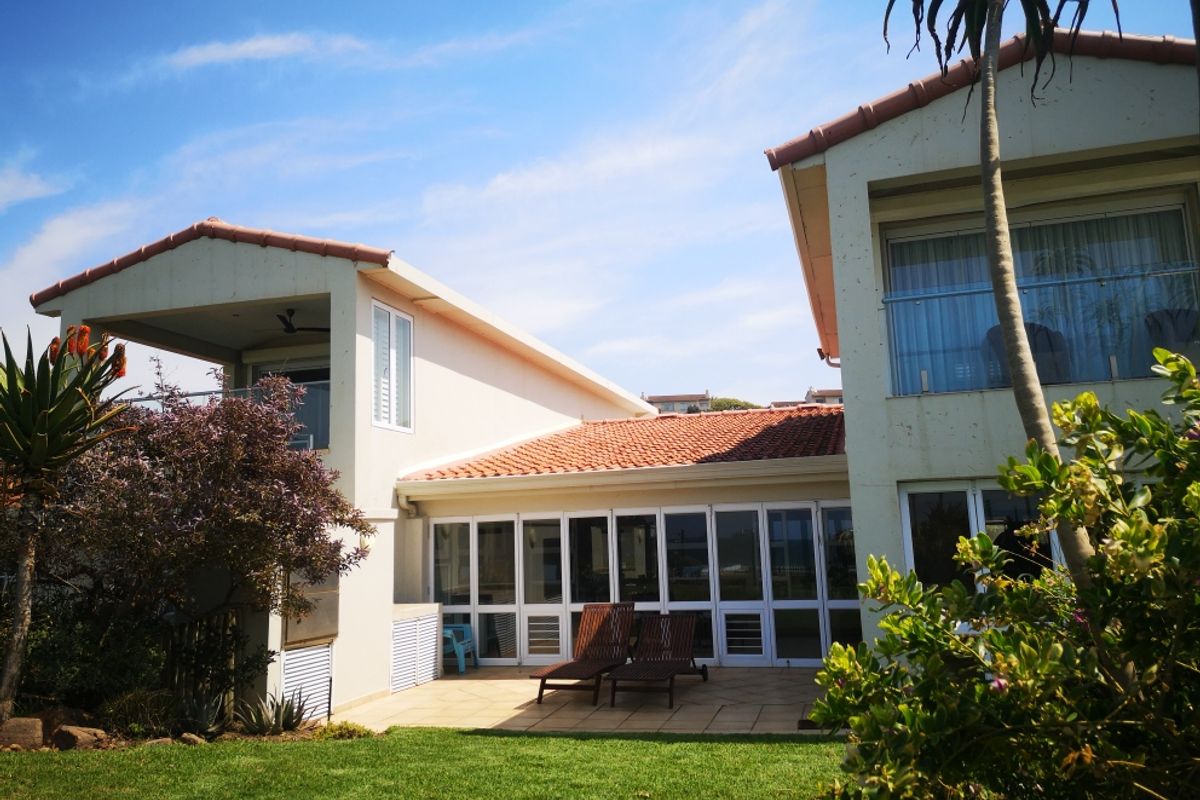 Rear view of the house featuring a tiled patio, glass sliding doors, and an upper-level balcony with a glass balustrade overlooking the garden.
