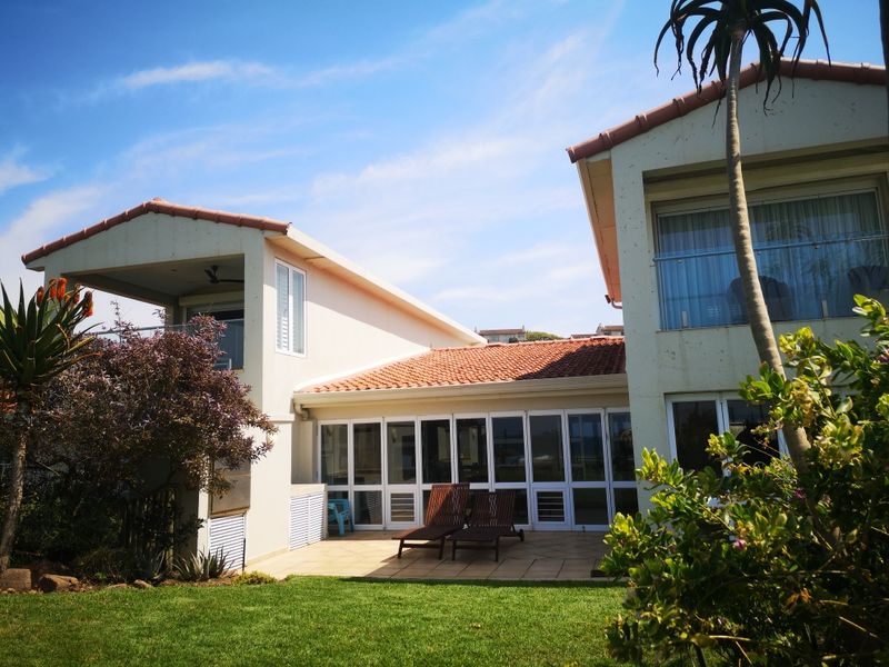 Rear view of the house featuring a tiled patio, glass sliding doors, and an upper-level balcony with a glass balustrade overlooking the garden.