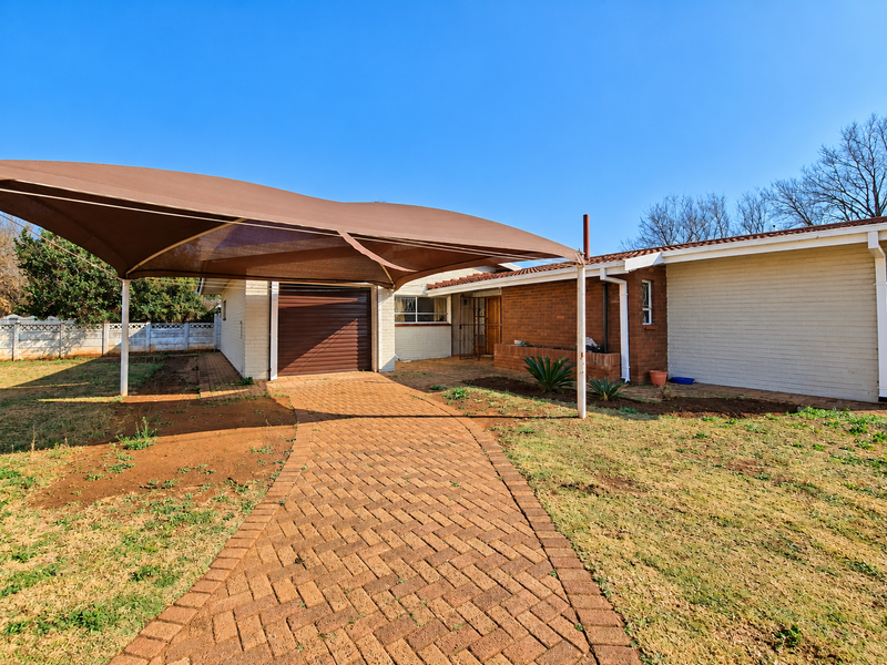 Front exterior view of the property featuring a brick paved driveway, a shade sail carport, and a single roll-up garage door.