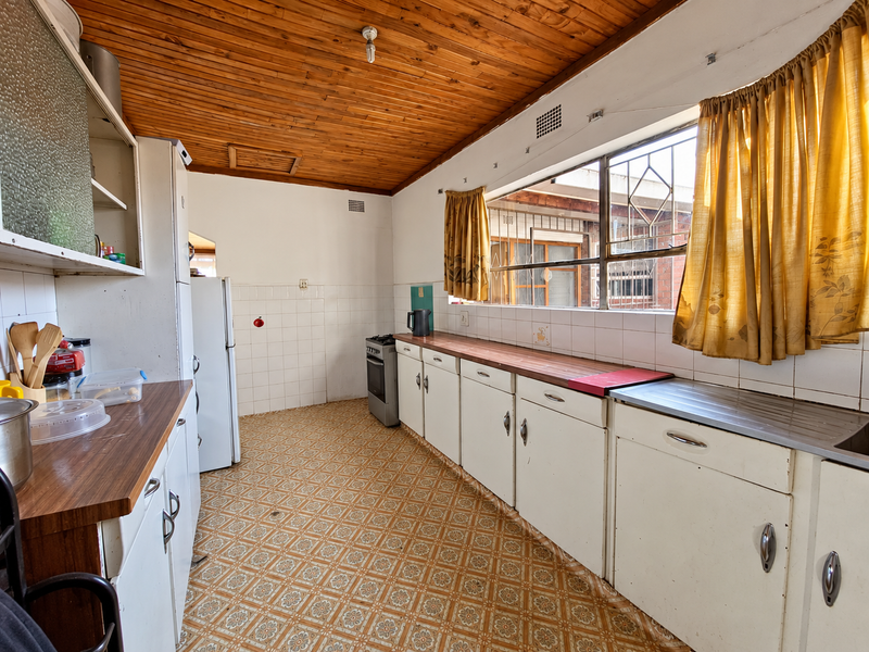 A dated kitchen featuring timber ceilings, original cabinetry, laminate countertops, and a freestanding stove, offering significant potential for a modern renovation.