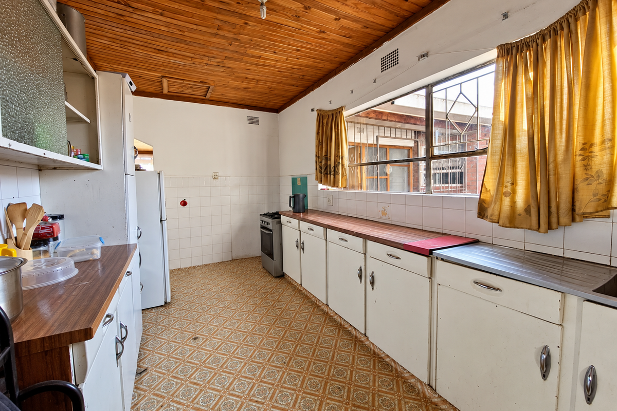 A dated kitchen featuring timber ceilings, original cabinetry, laminate countertops, and a freestanding stove, offering significant potential for a modern renovation.